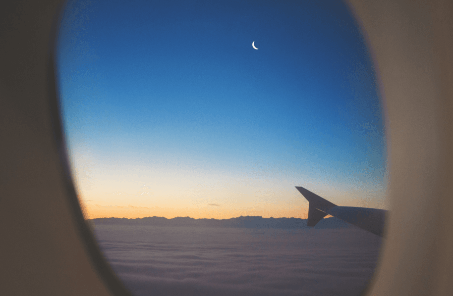 A photo taken through the window of an airplane of a blue sky with the moon showing.