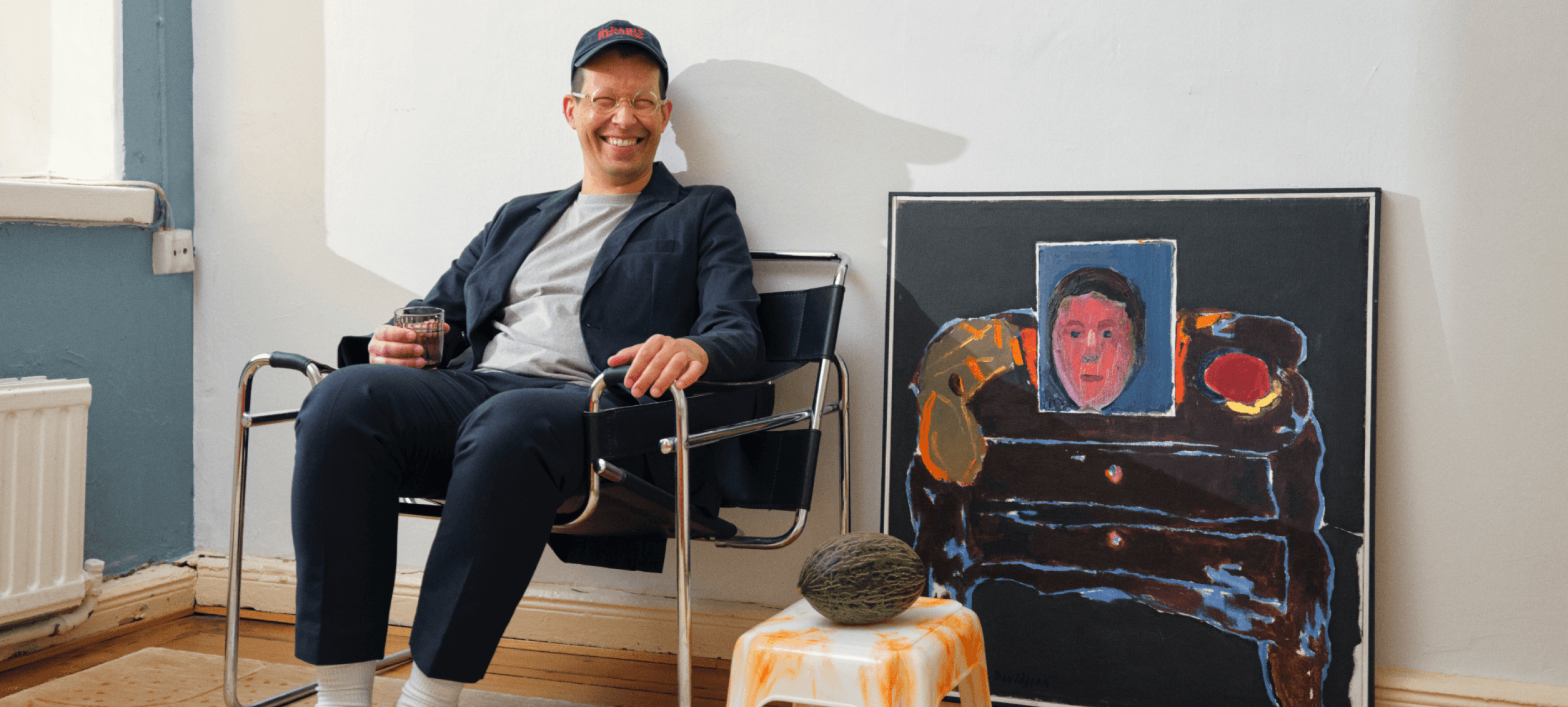 Smiling person sitting down next to painting.