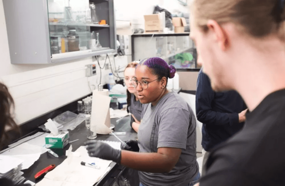 A person talking in a lab with surrounding people listening.